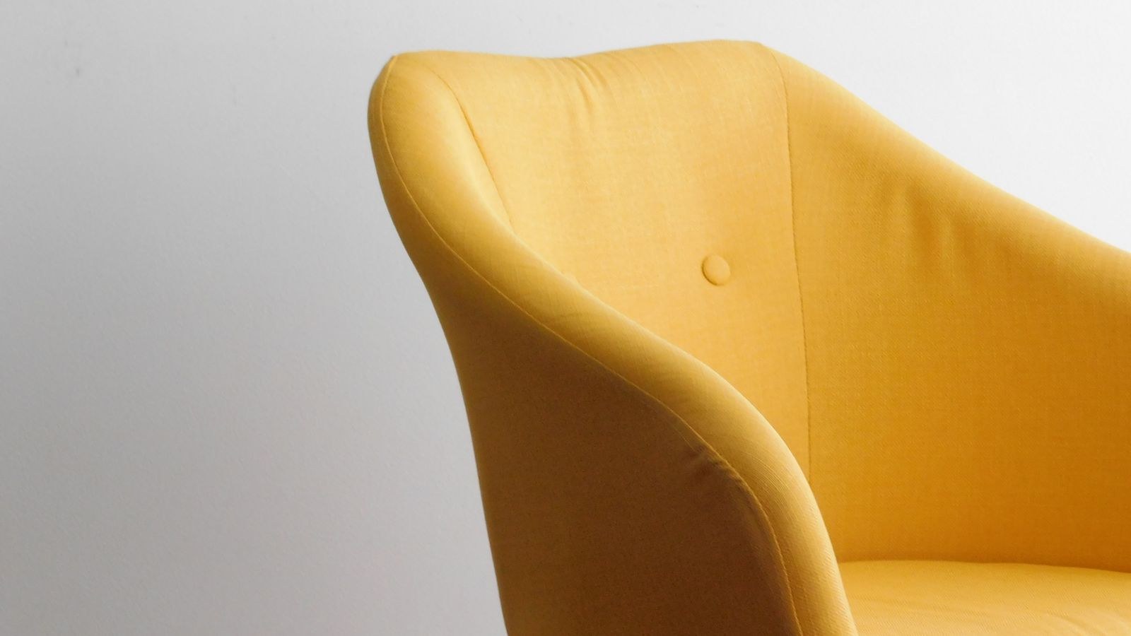 Yellow upholstered accent chair against a minimalist wall