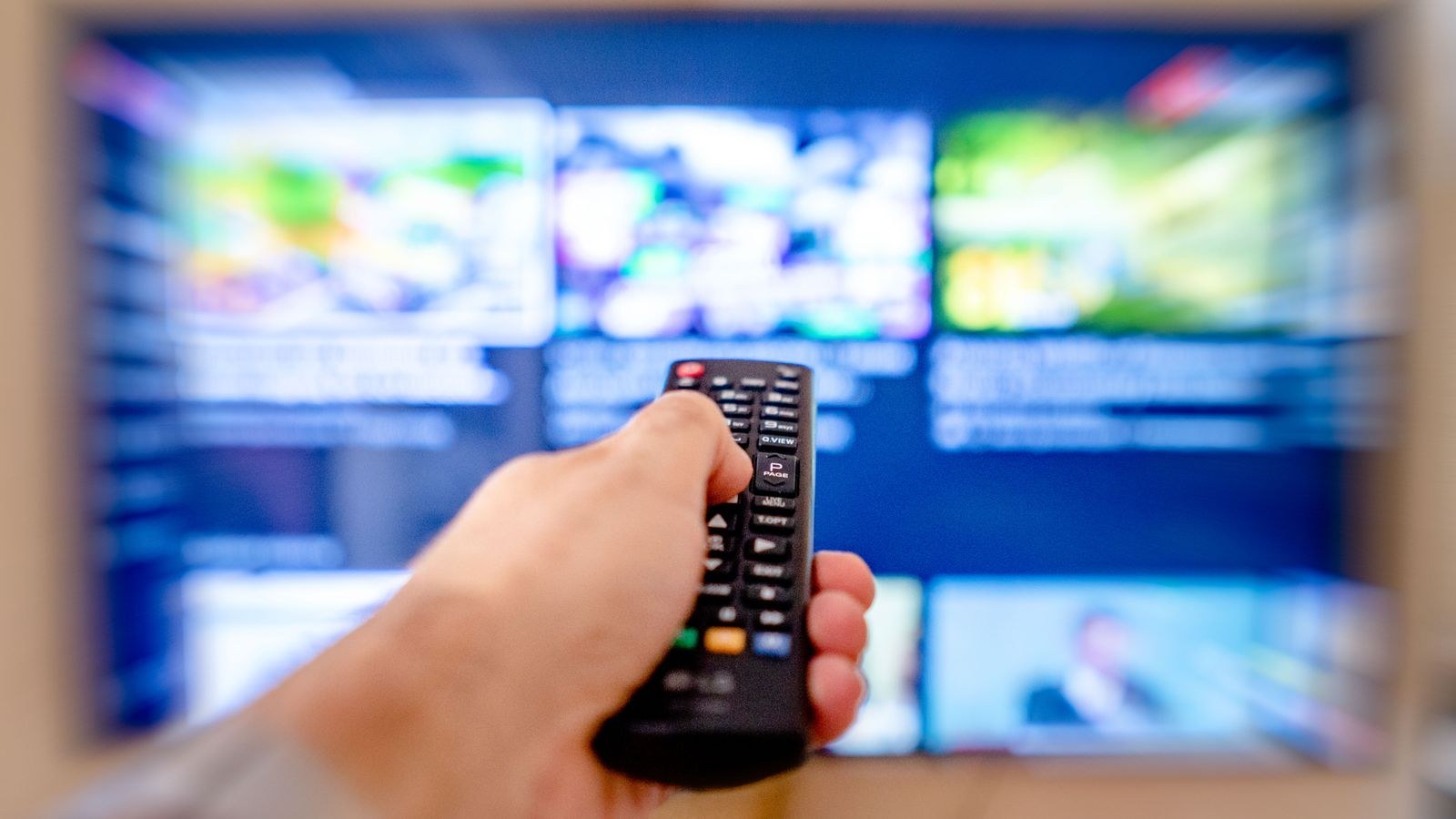 Hand using a remote control to navigate a television streaming interface