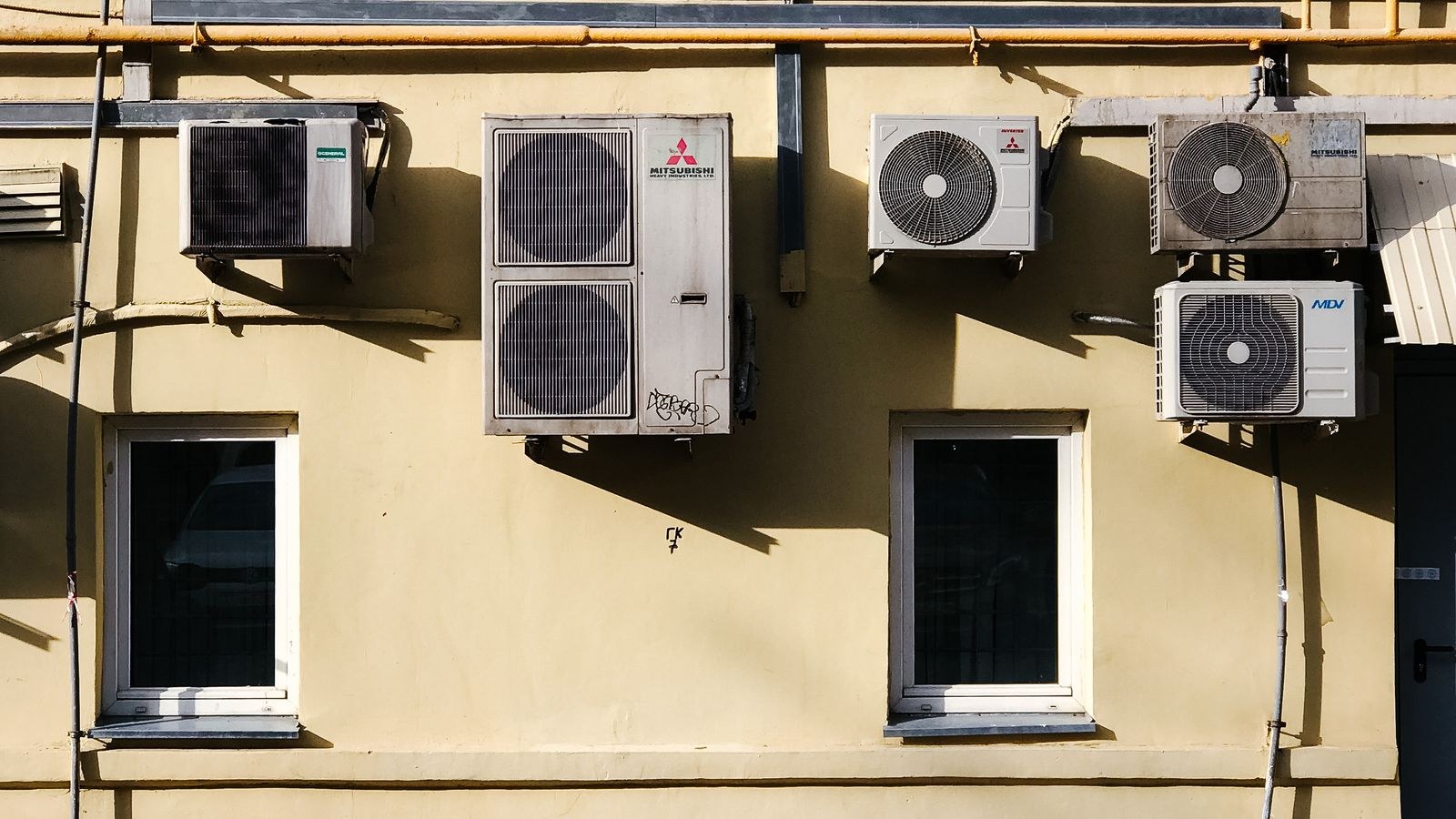 Yellow building facade with multiple air conditioning units mounted on the wall