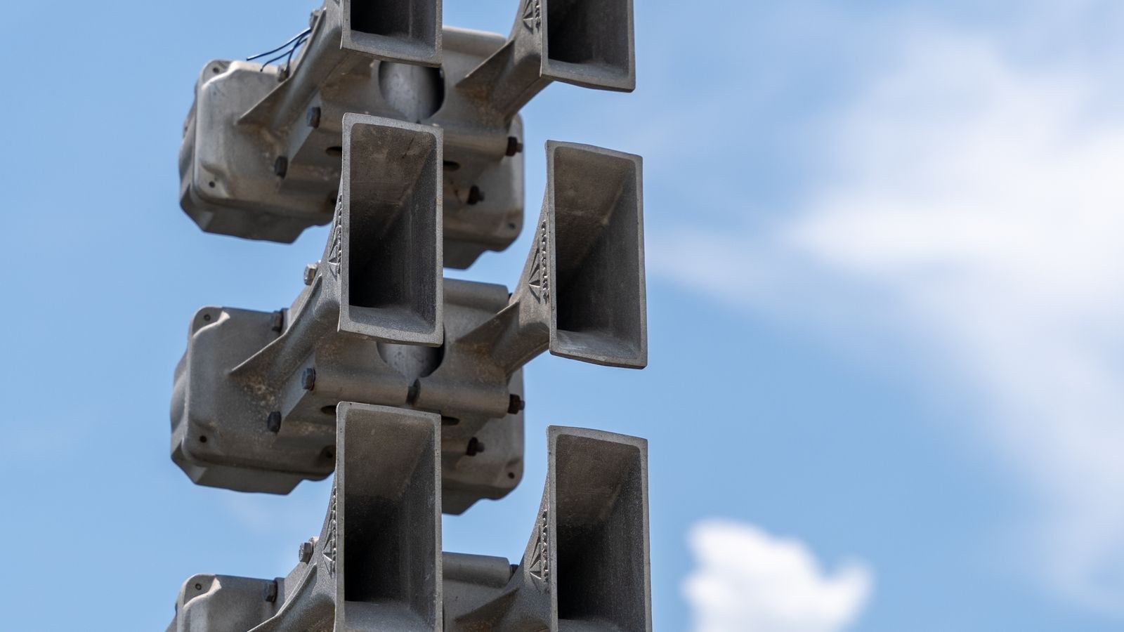 Outdoor warning sirens mounted high on a pole against a clear sky