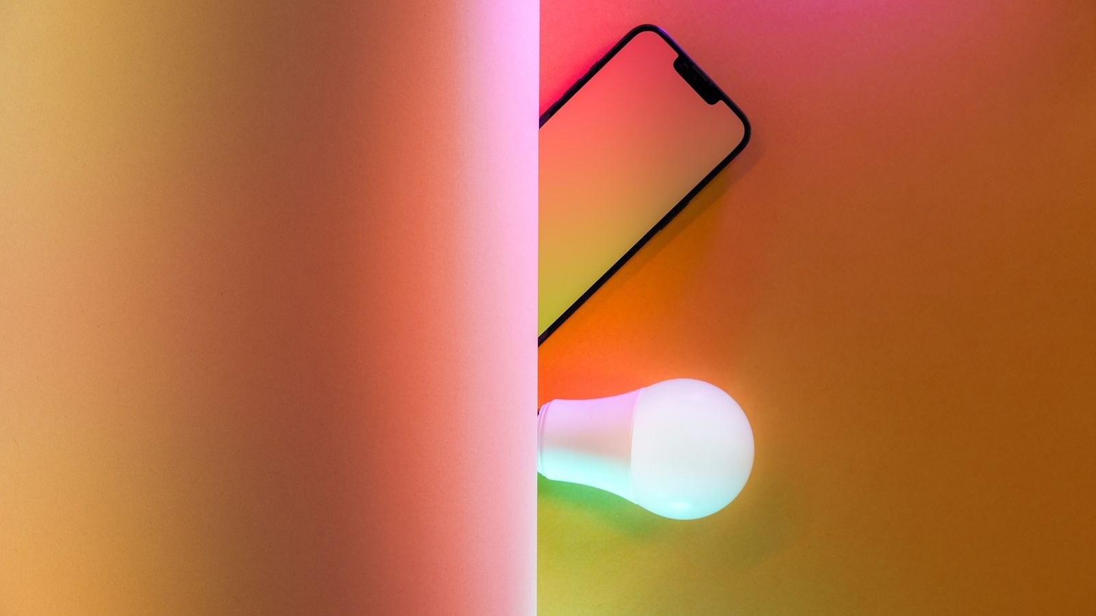 Smart light bulb glowing in color beside a smartphone app