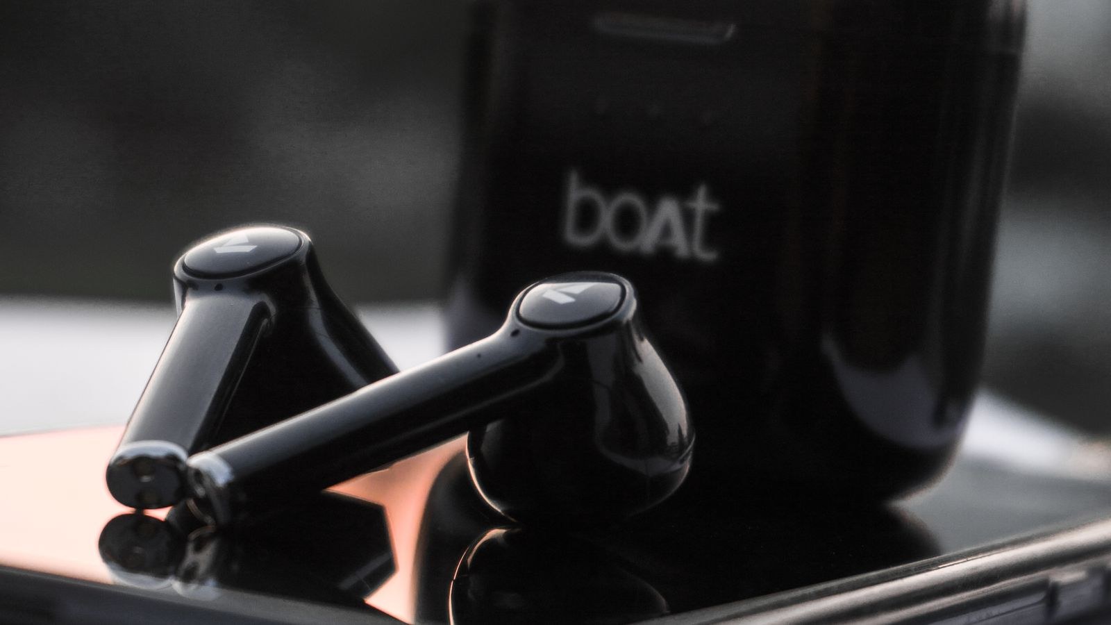 Black wireless earbuds resting on a smartphone with a blurred outdoor background