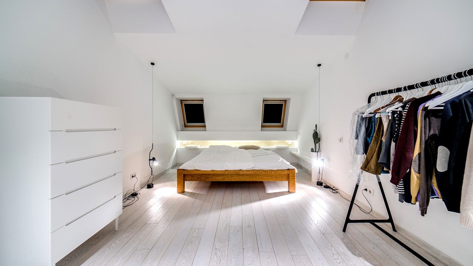 Minimalist white bedroom with a low wooden platform bed frame under skylights