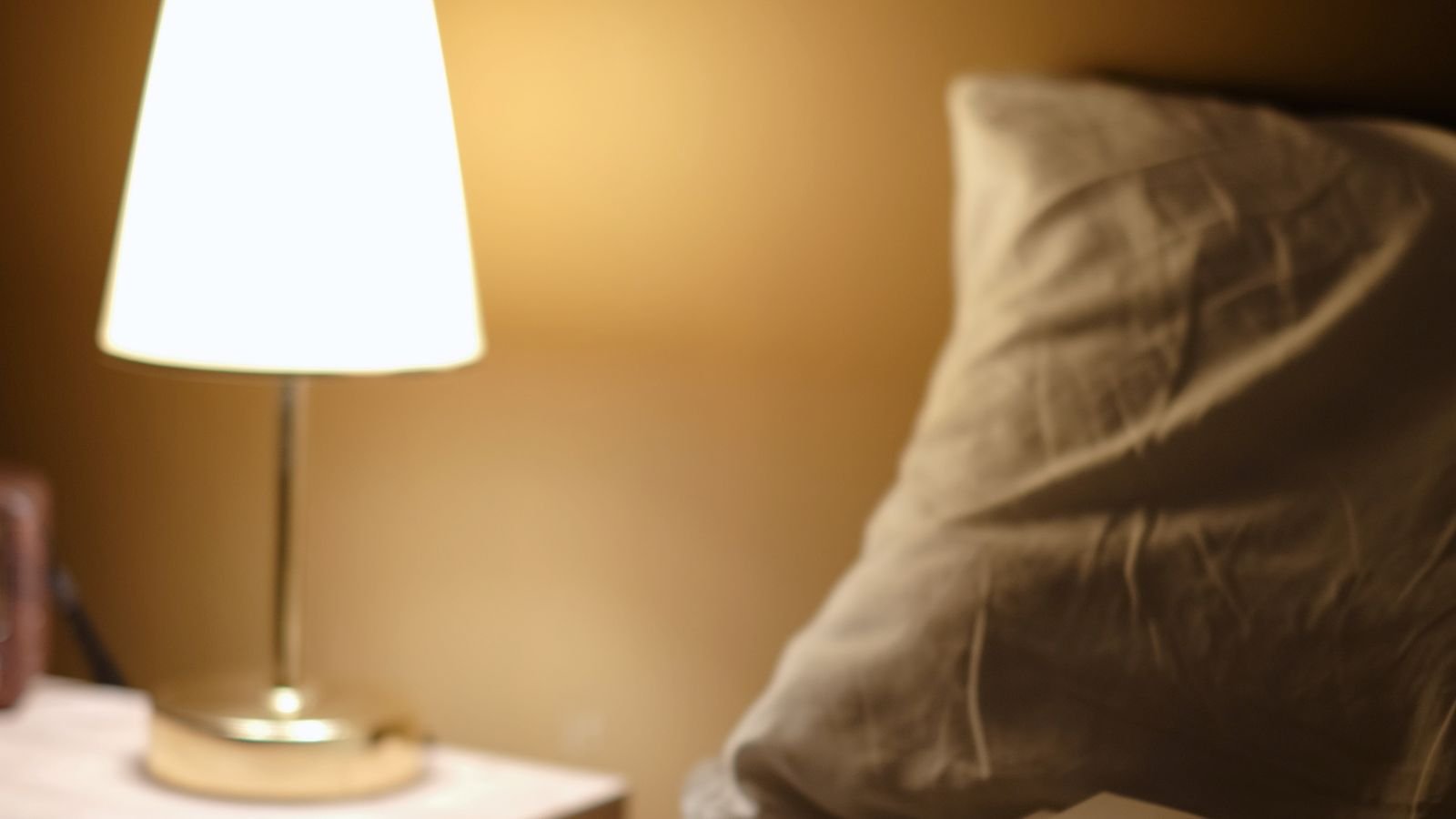 Bedside table with open books and a lit reading lamp at night