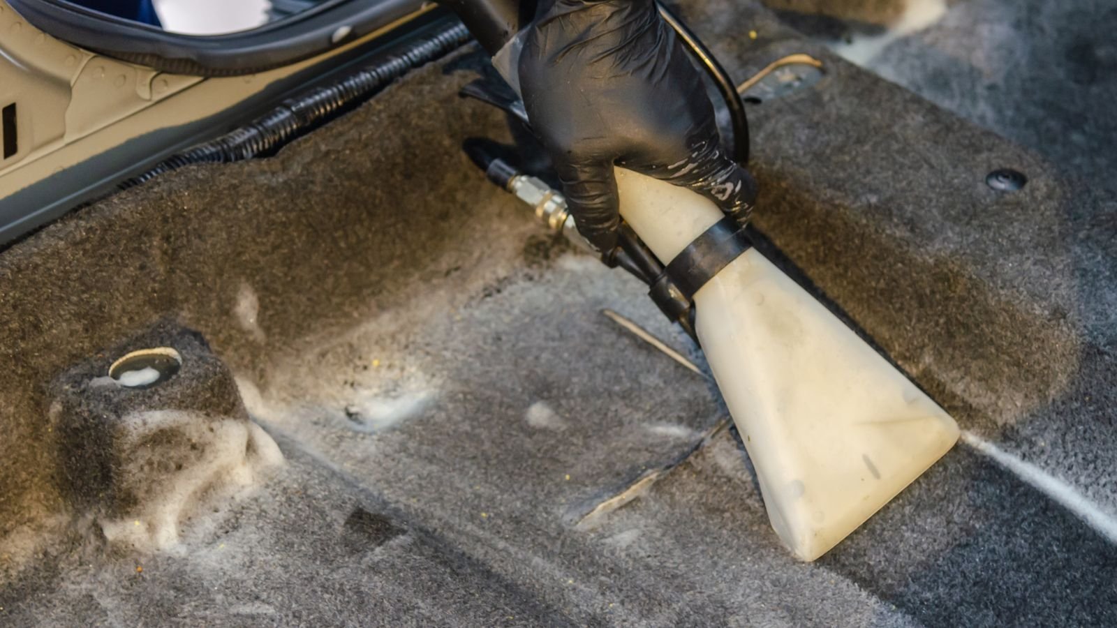 Person vacuuming a car interior carpet with a handheld vacuum nozzle