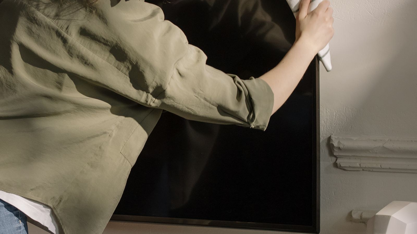 Woman wiping a television screen with a microfibre cloth in a modern living room