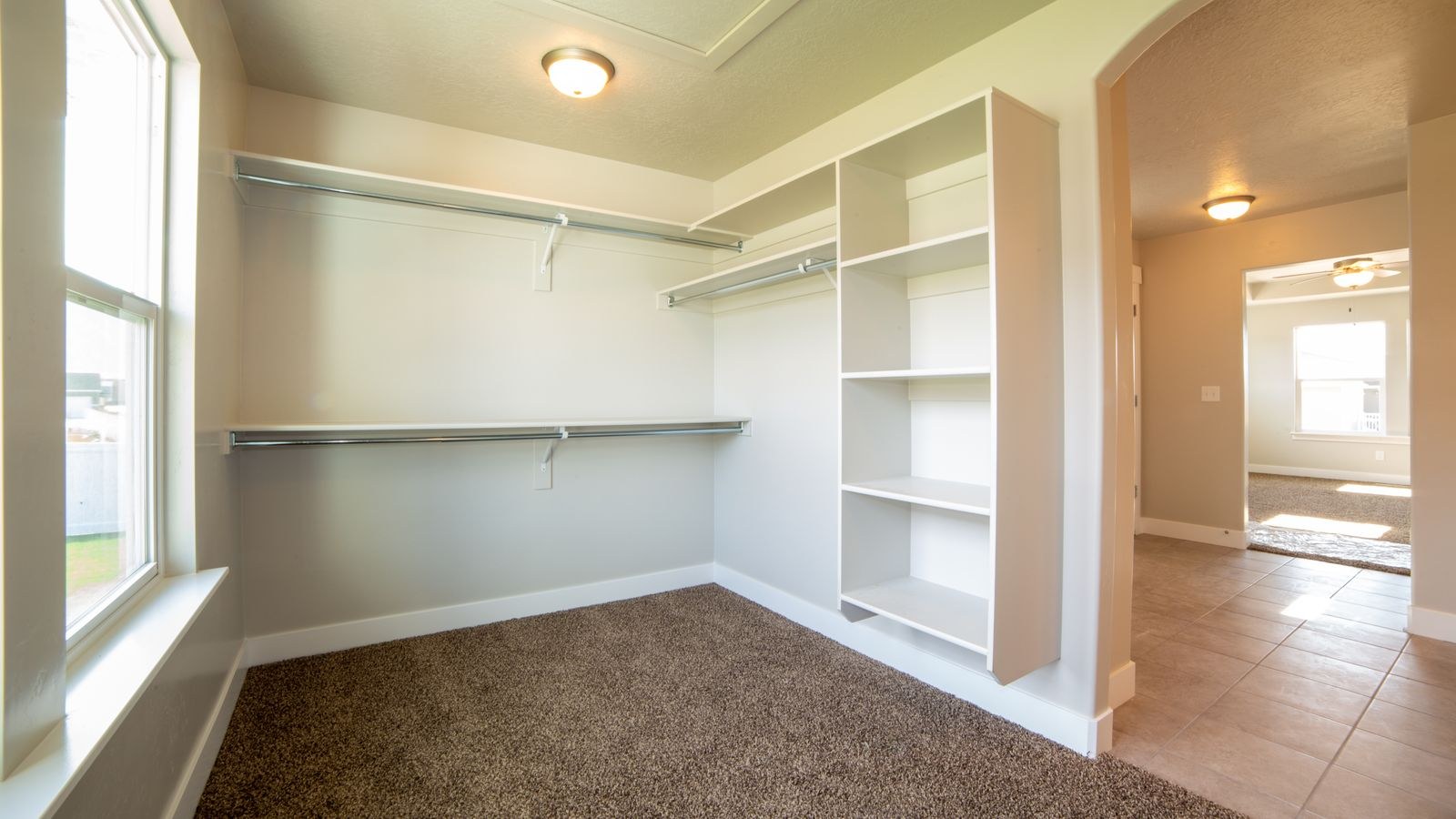 Reach-in closet with hanging clothes illuminated by an overhead LED fixture