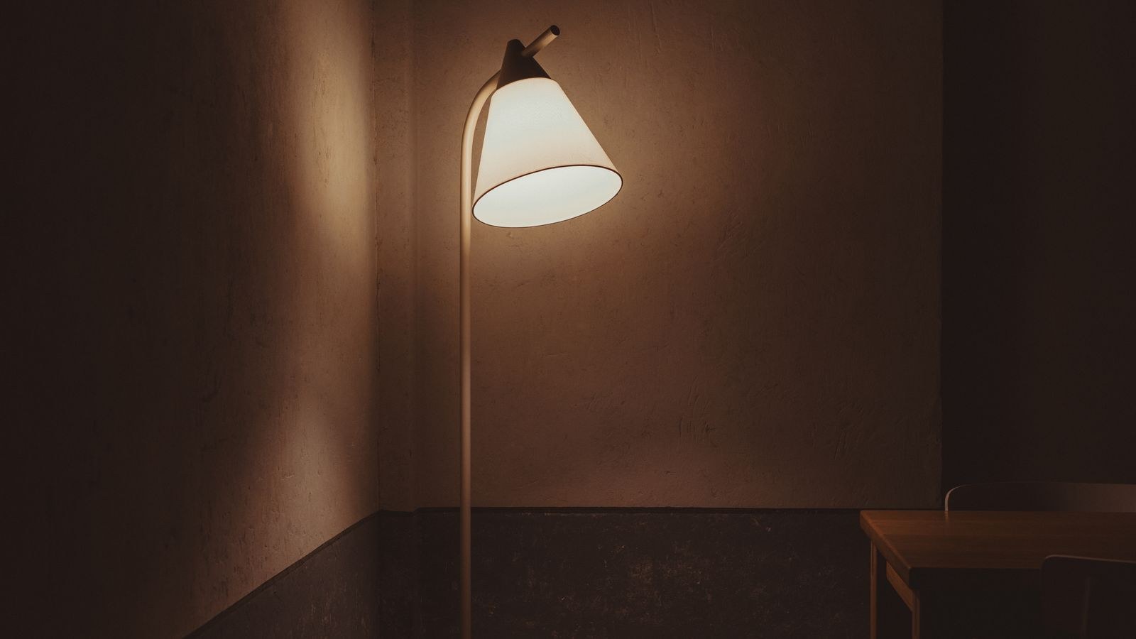 Minimalist dark room brightened by a glowing floor lamp beside a wooden table