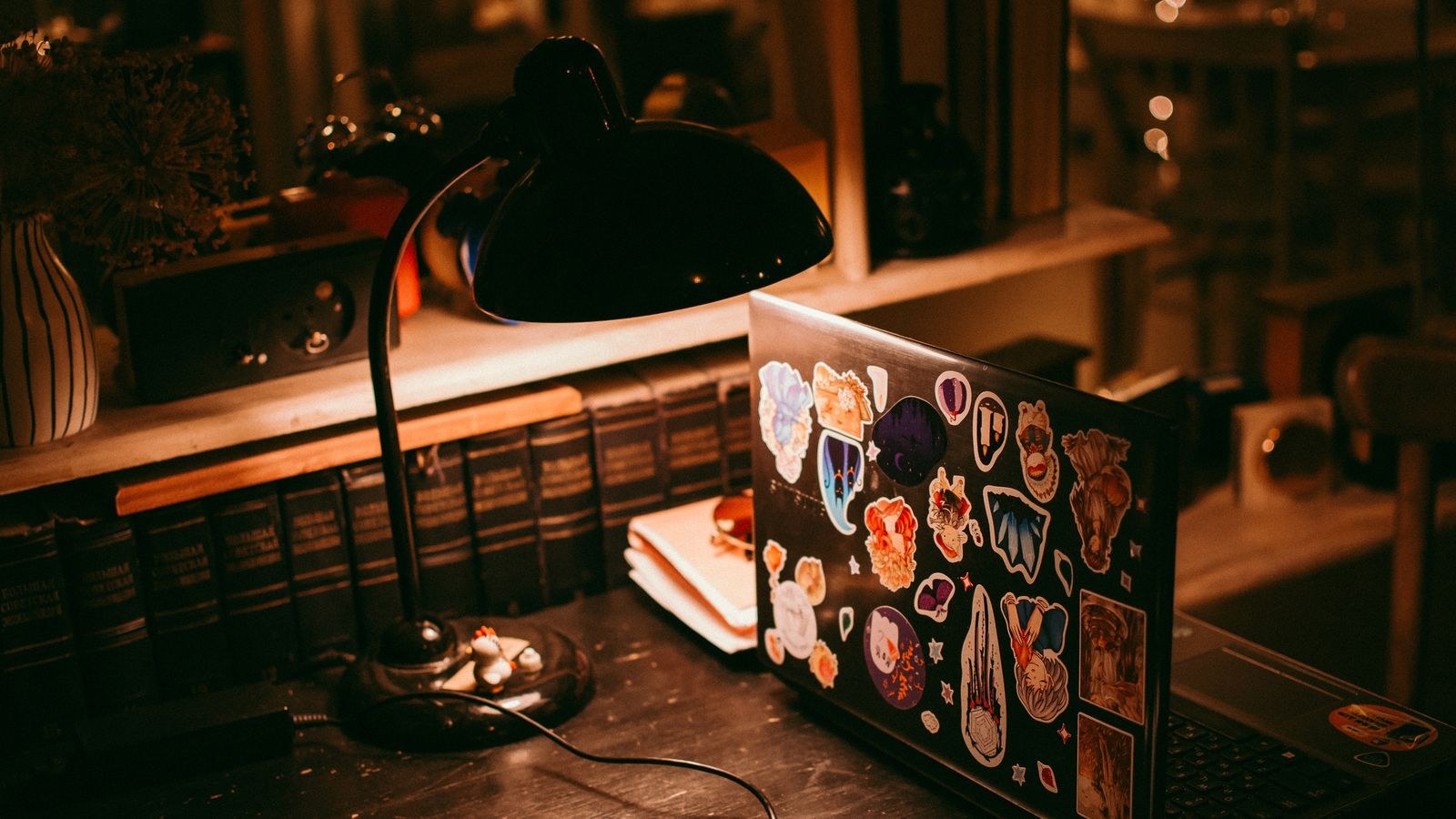 Warm desk lamp lighting a workspace with a laptop and stacked books