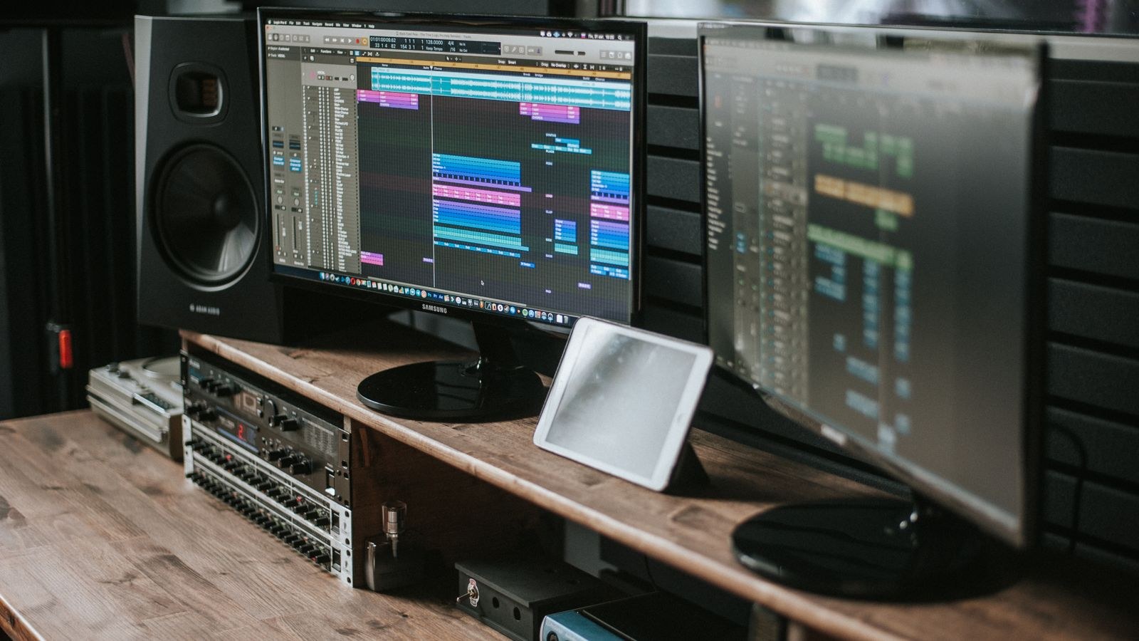 Studio monitor speakers beside dual screens running audio editing software