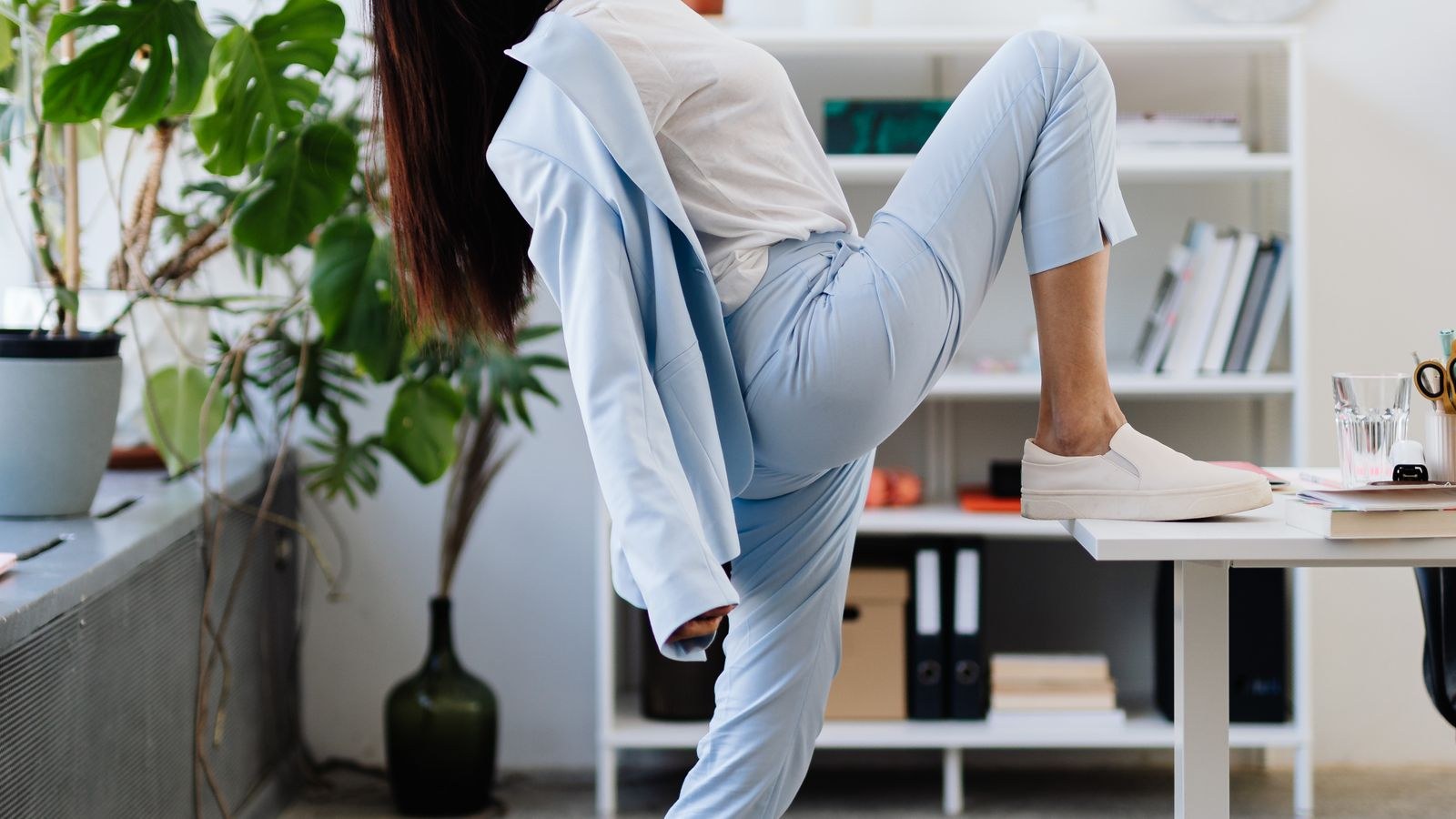 Professional woman stretching her arms and shoulders beside a desk in a bright office