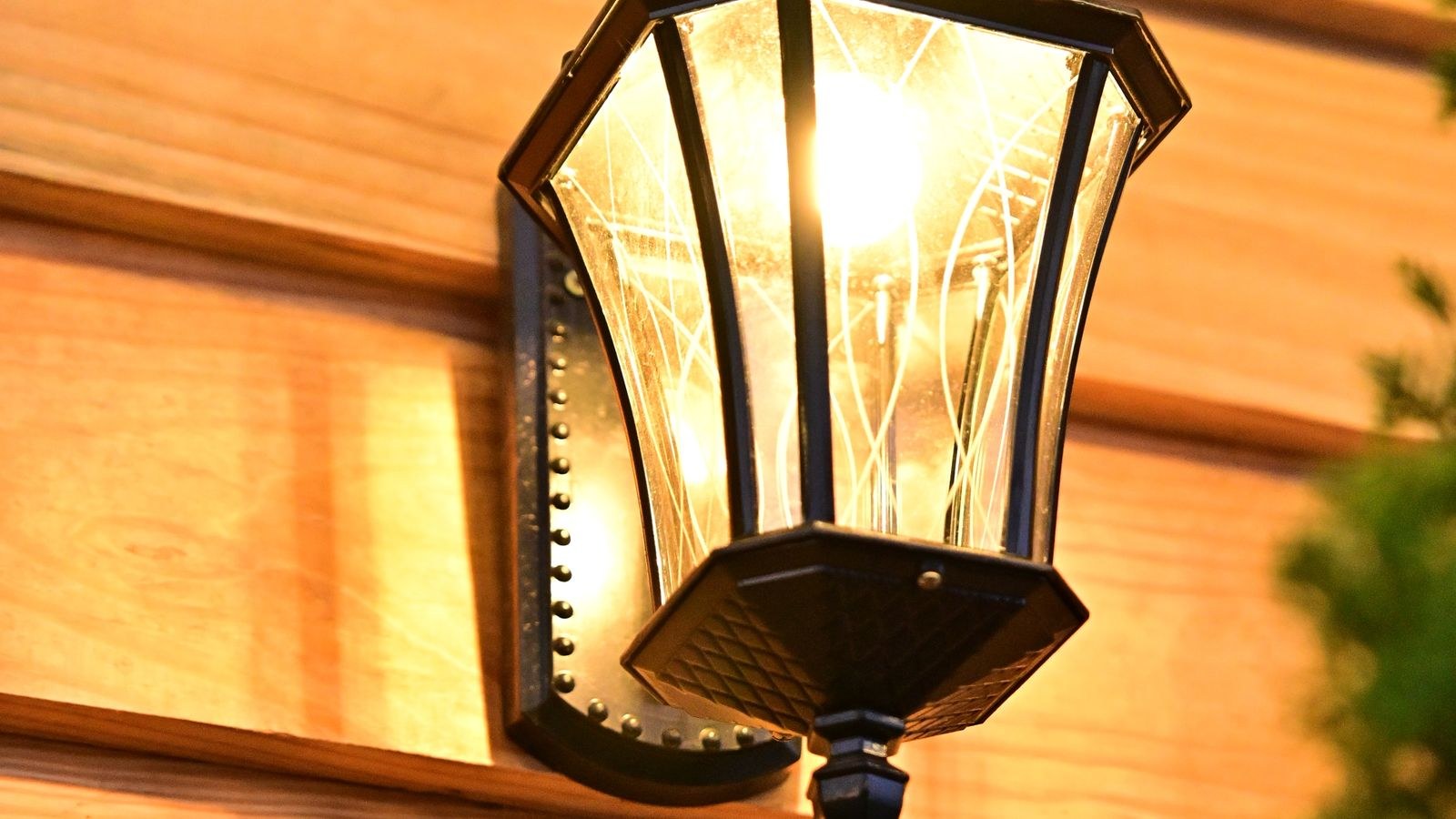 Outdoor wall lantern mounted beside a wooden exterior wall at dusk