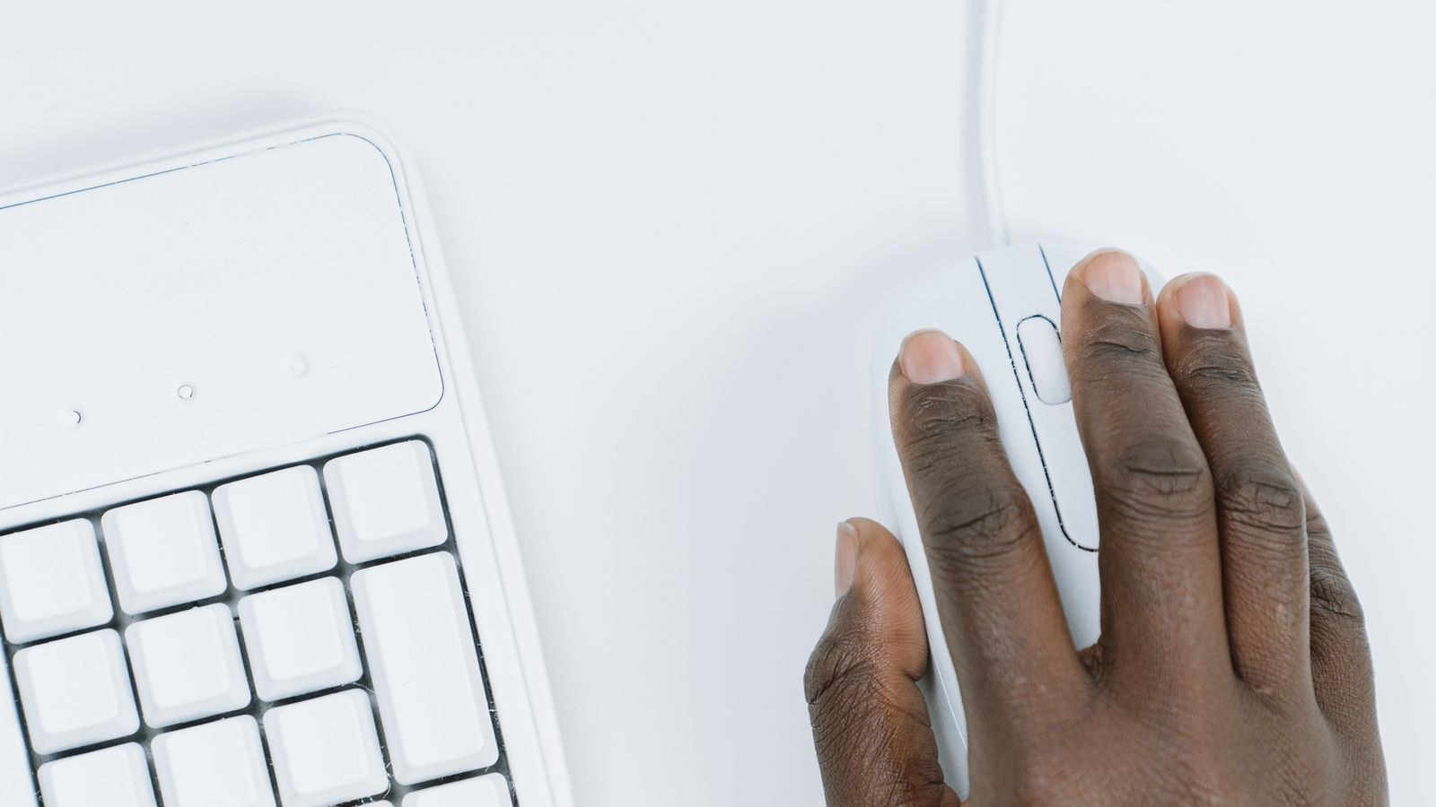 Hand resting on a computer mouse beside a keyboard on a white desk