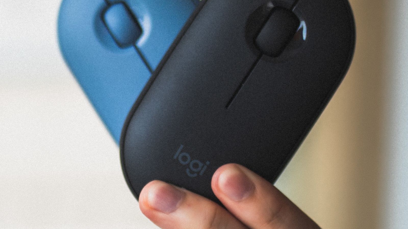 Hand holding several modern wireless mice of different shapes and colours
