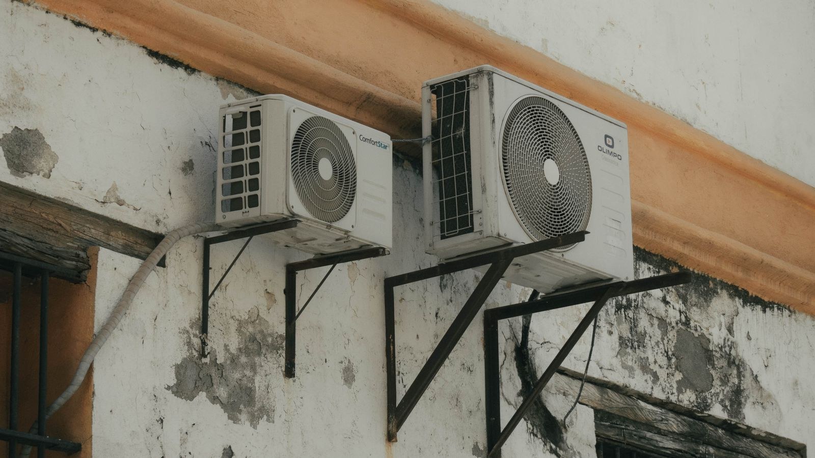 Two outdoor AC condenser units installed on a weathered concrete wall