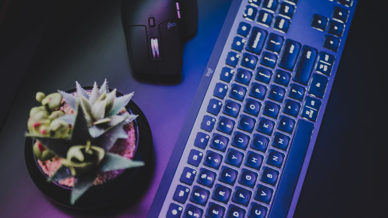 Modern wireless keyboard with colourful backlighting placed near a mouse on a desk