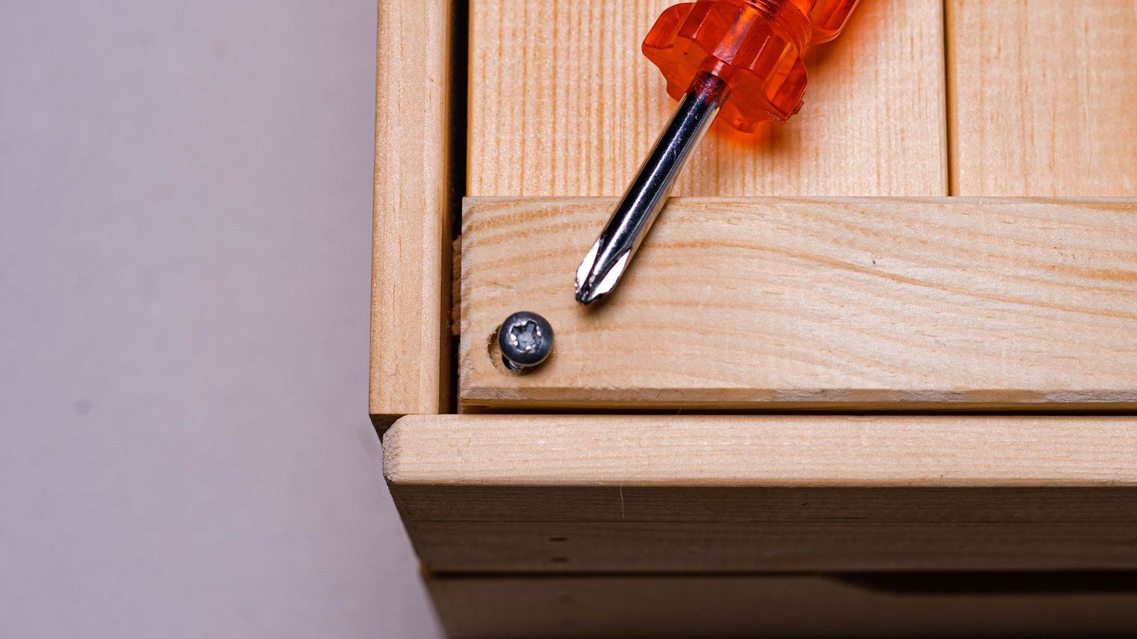 Screwdriver and screw on a wooden panel during furniture repair