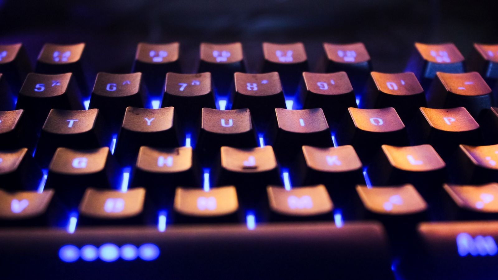 Backlit computer keyboard glowing with blue lighting on a desk