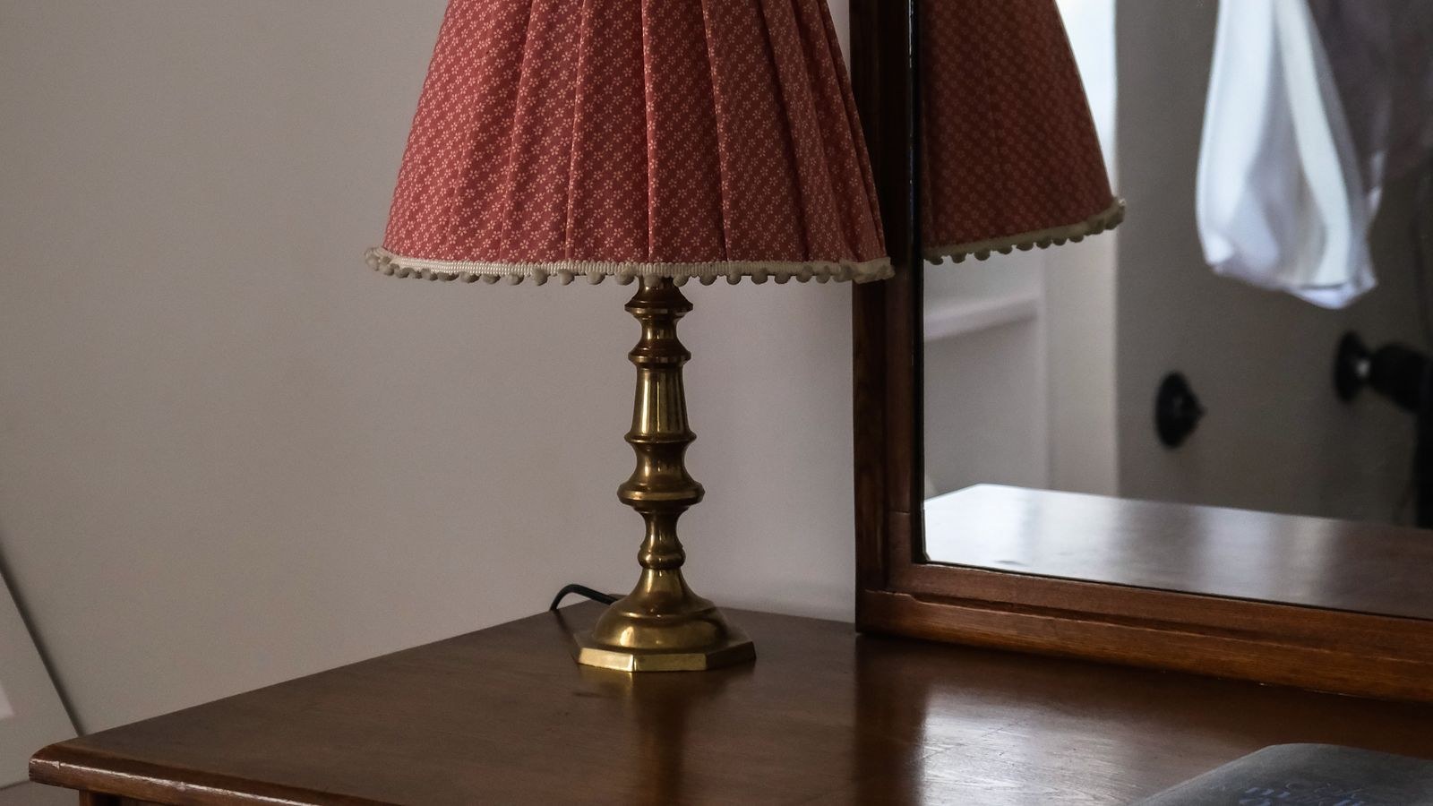 Tall wooden dresser with a lamp and mirror in a bedroom