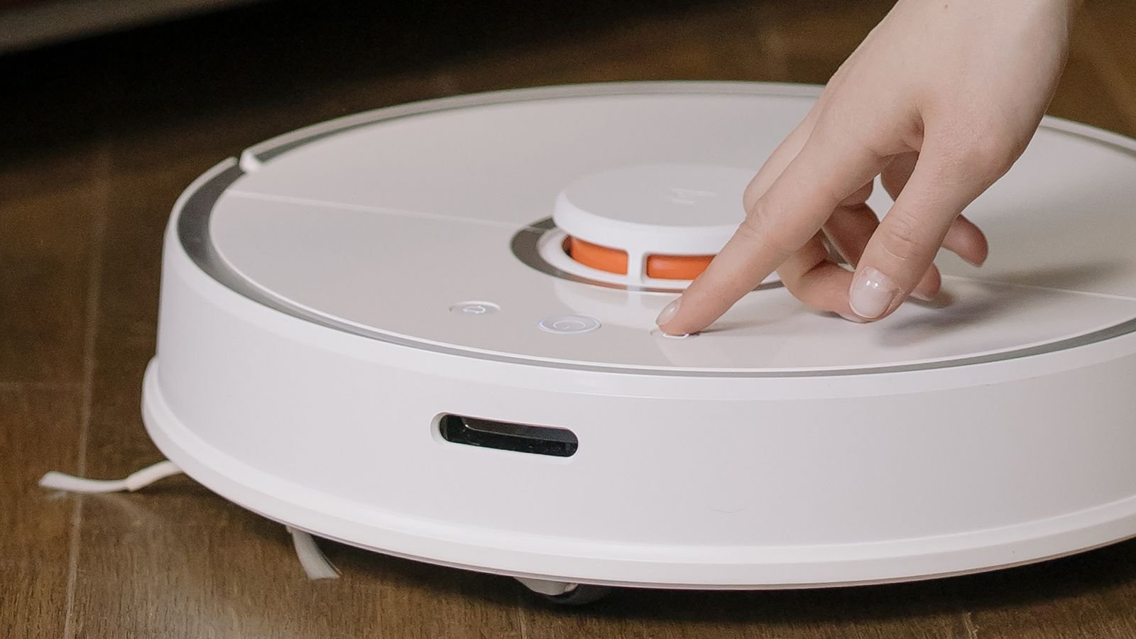 Hand pressing the button on a robotic vacuum cleaner during maintenance