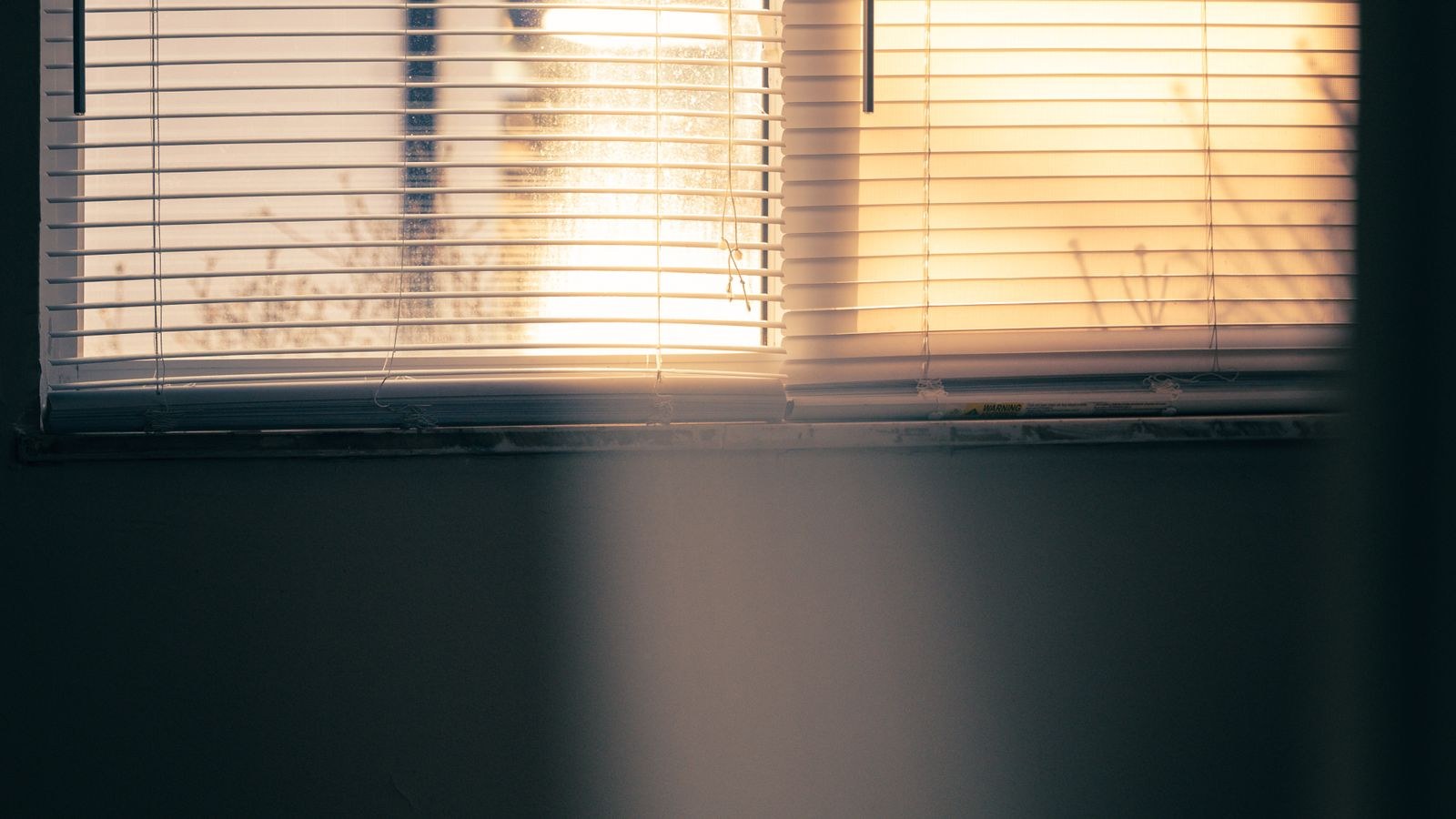 Soft daylight casting shadows through window blinds in a hot upstairs bedroom