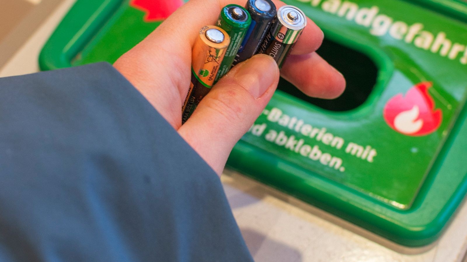 Hand placing used batteries into a battery recycling bin