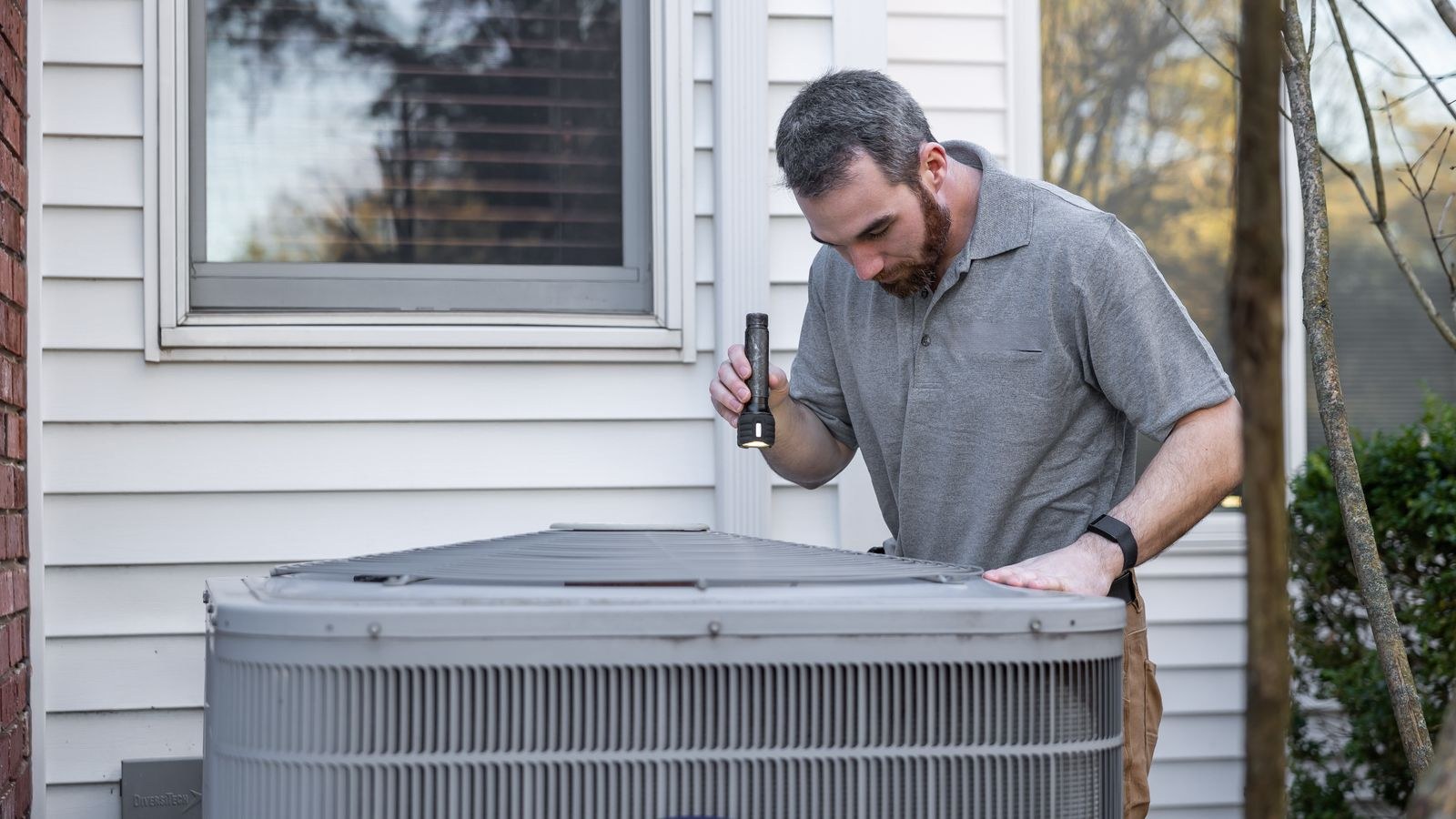 Technician inspecting an air conditioning unit for maintenance and drainage