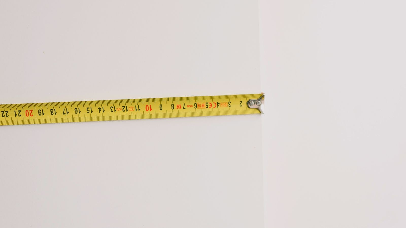 Yellow measuring tape against a wall during home measuring for new furniture