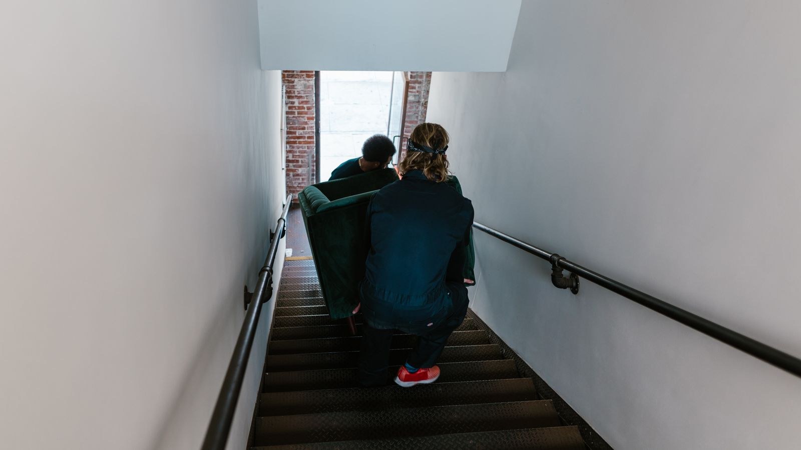 Movers carefully carrying a couch down an indoor staircase