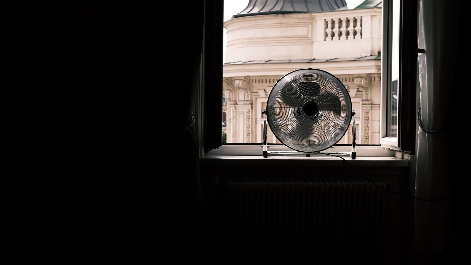 Fan placed on a windowsill exhausting hot air out of a room toward the street