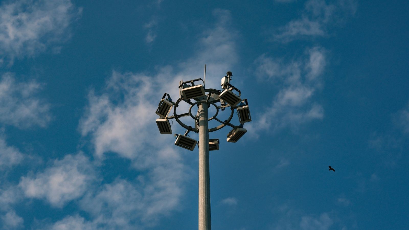 Outdoor floodlights mounted high on a pole against a blue sky
