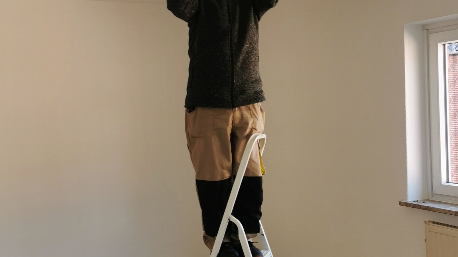 Person on a ladder working on a ceiling mounted device in an empty room