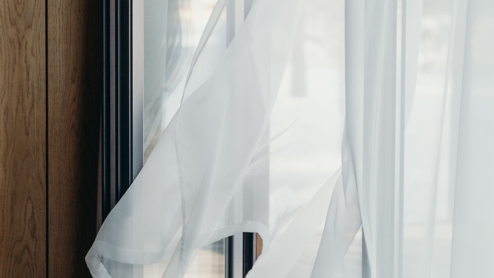 White curtains beside a secured sliding glass door in a minimalist room