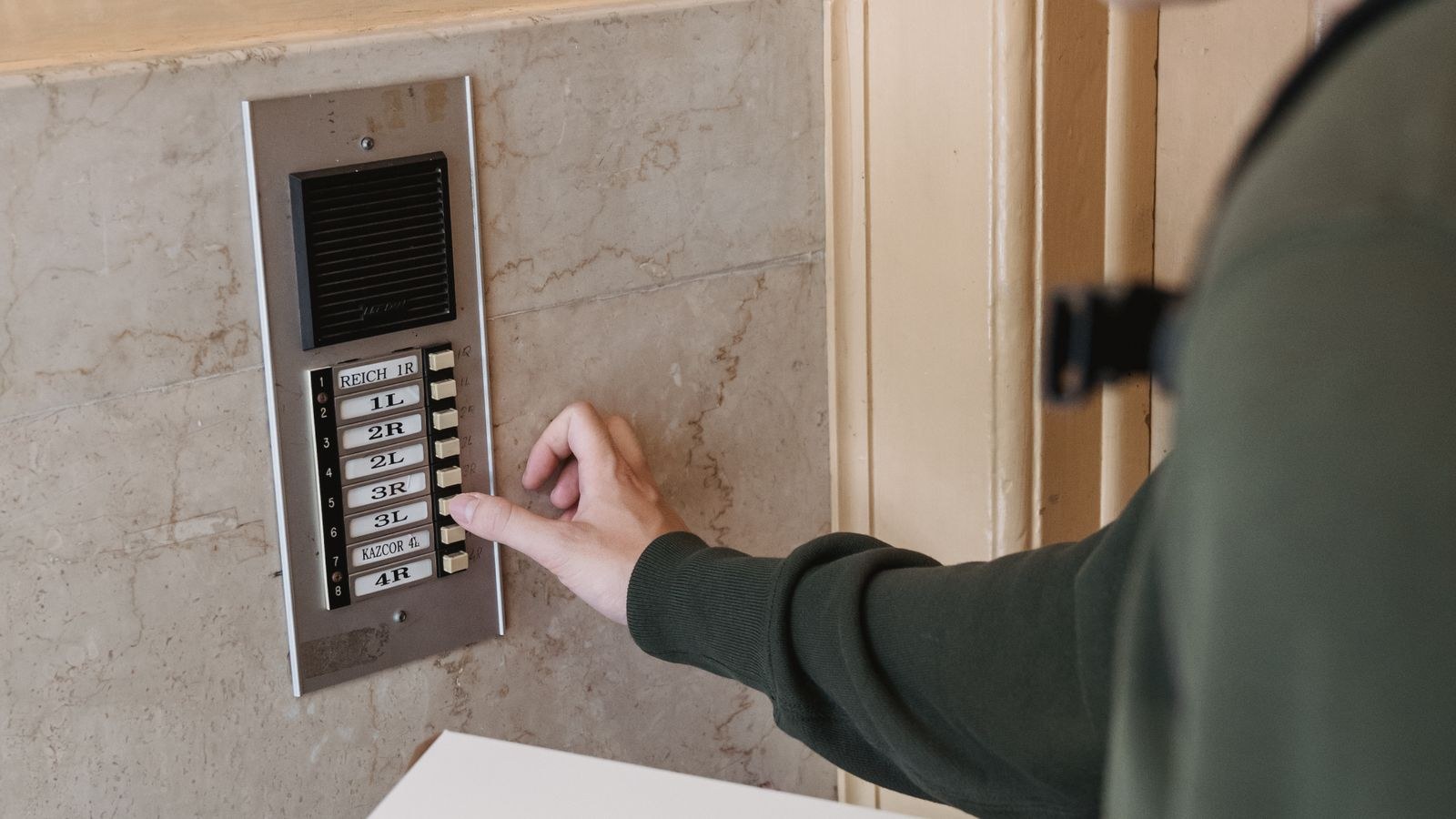Delivery courier pressing an apartment doorbell while holding a package