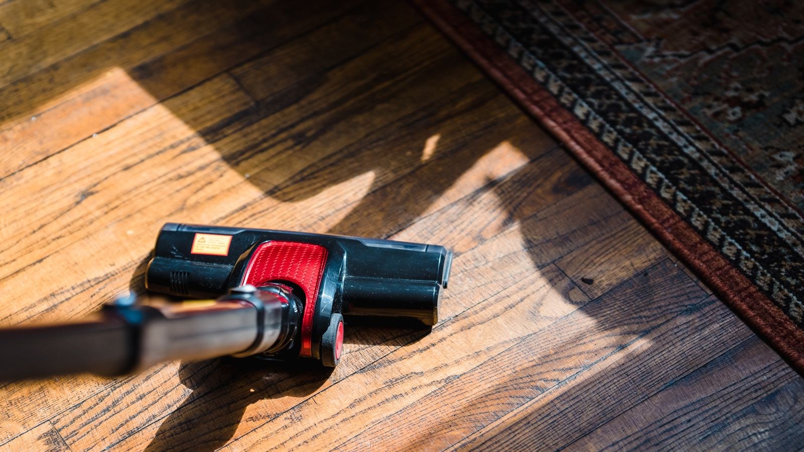 Vacuum cleaner beside a patterned rug edge on a wooden floor