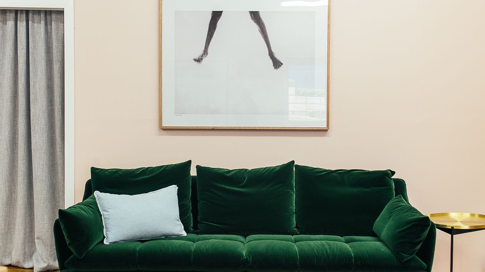 Green velour sofa with cushions and a small round table on a parquet floor