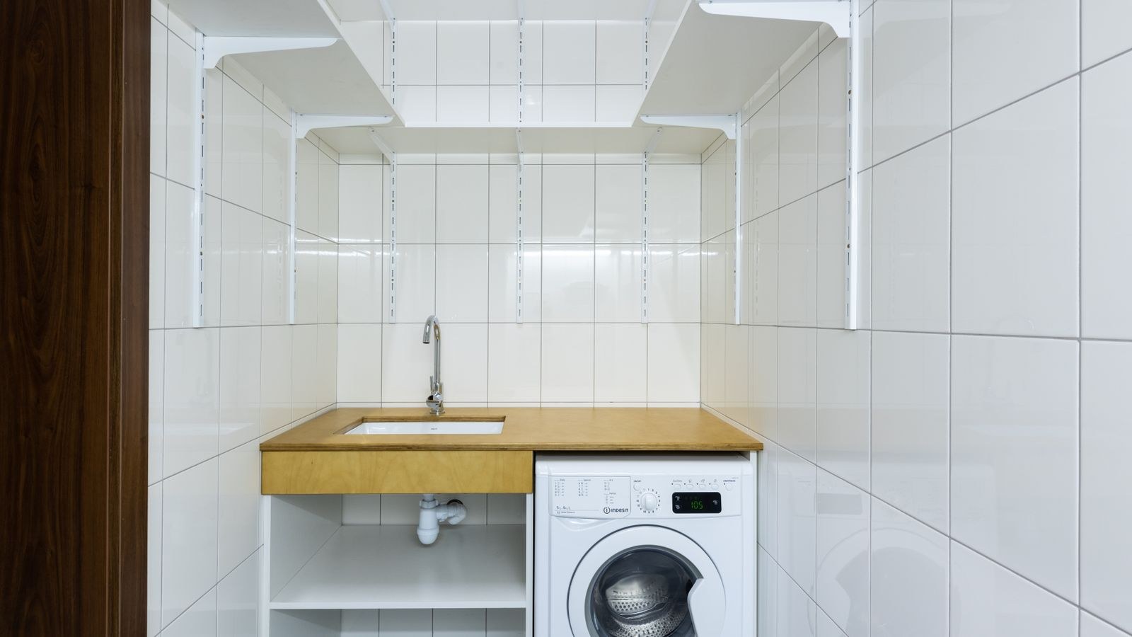 Modern laundry area with a white washing machine against tiled walls