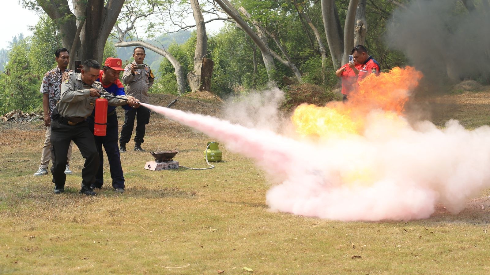Group learning to aim a fire extinguisher at the base of a training fire outdoors