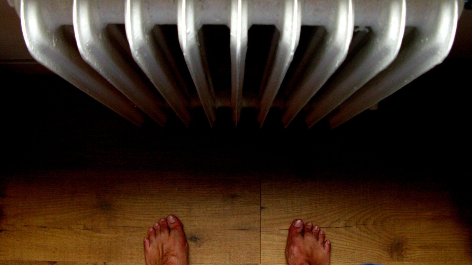 Bare feet on a wooden floor beside a warm radiator in a heated room