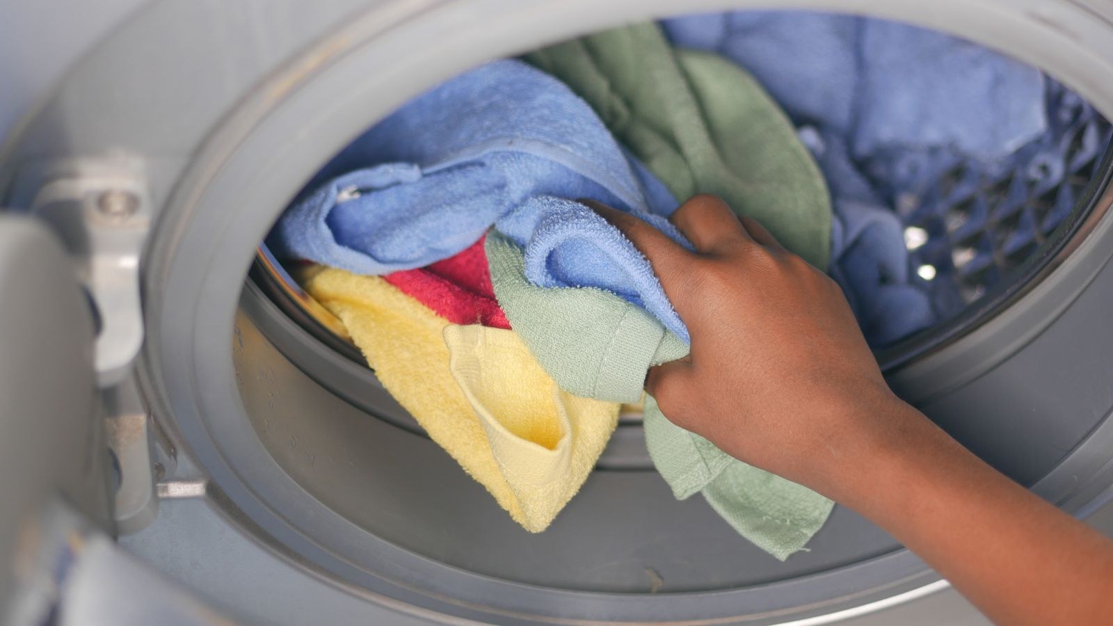 Hand loading colourful towels into a front-loading washing machine