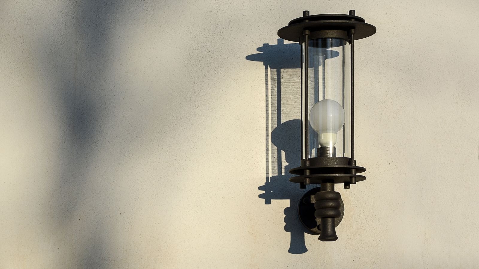 Outdoor wall light fixture casting light on a textured exterior wall at dusk