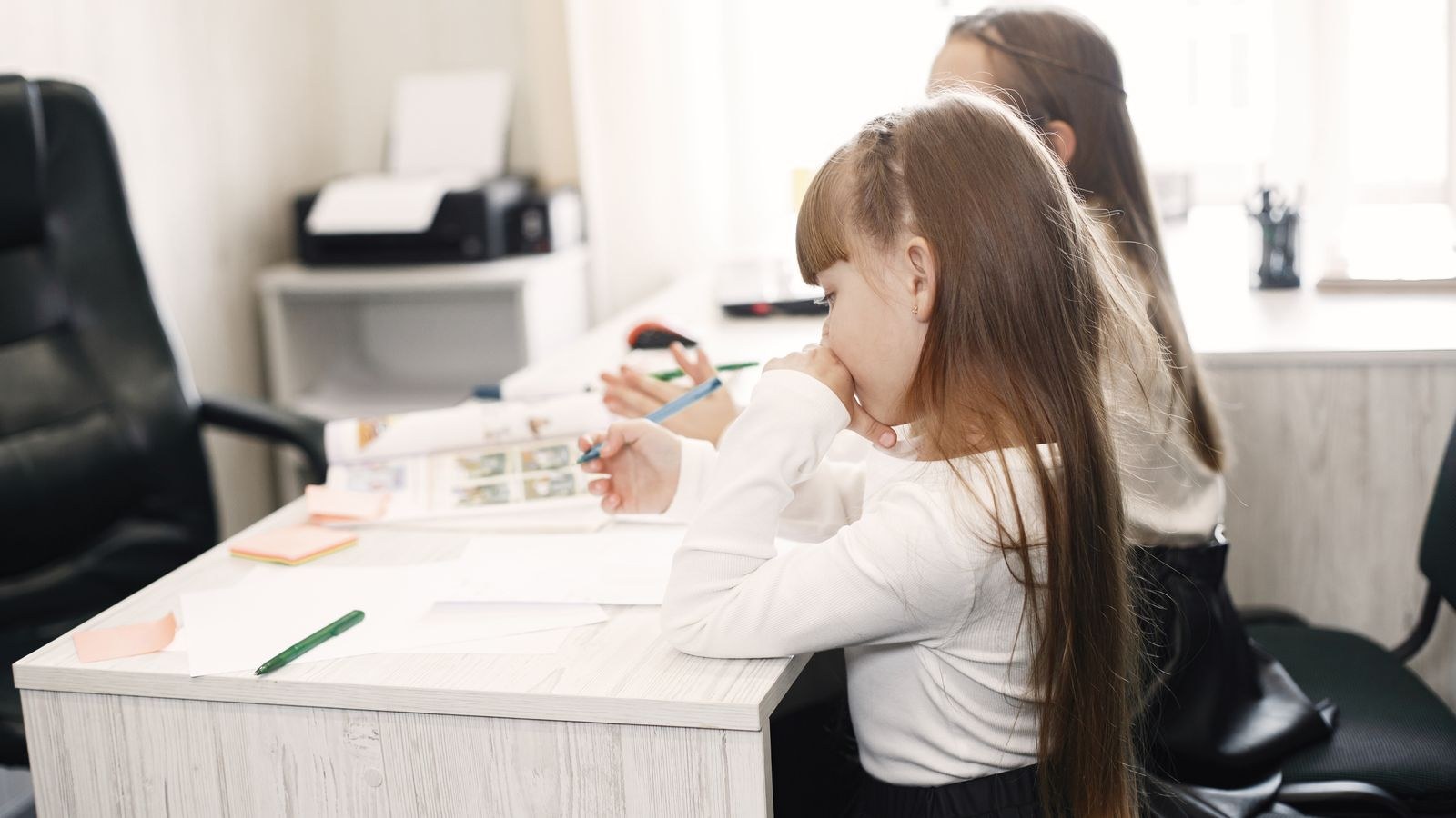 Girl seated at a correctly sized study desk doing homework with materials spread out