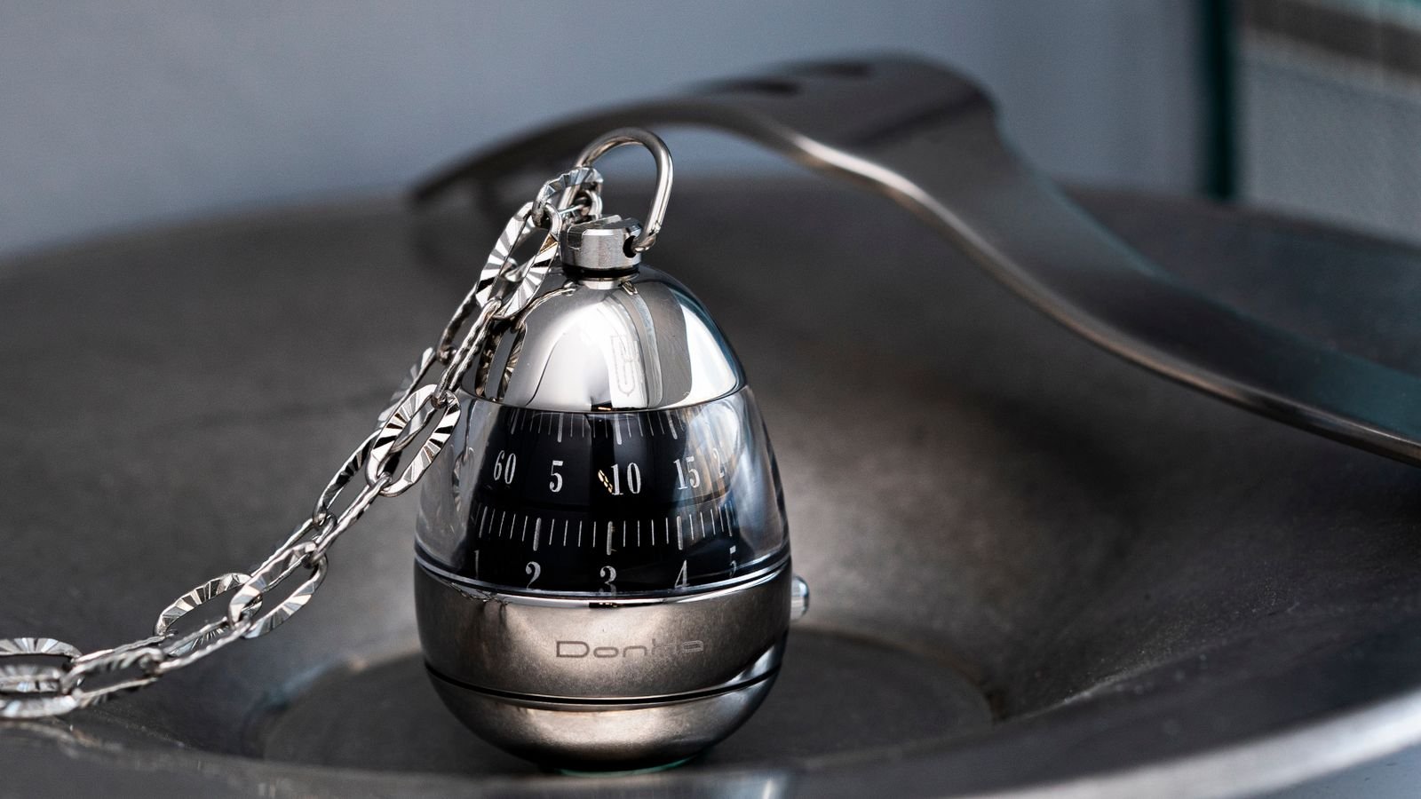 Stainless steel egg-shaped kitchen timer close up on a metal surface