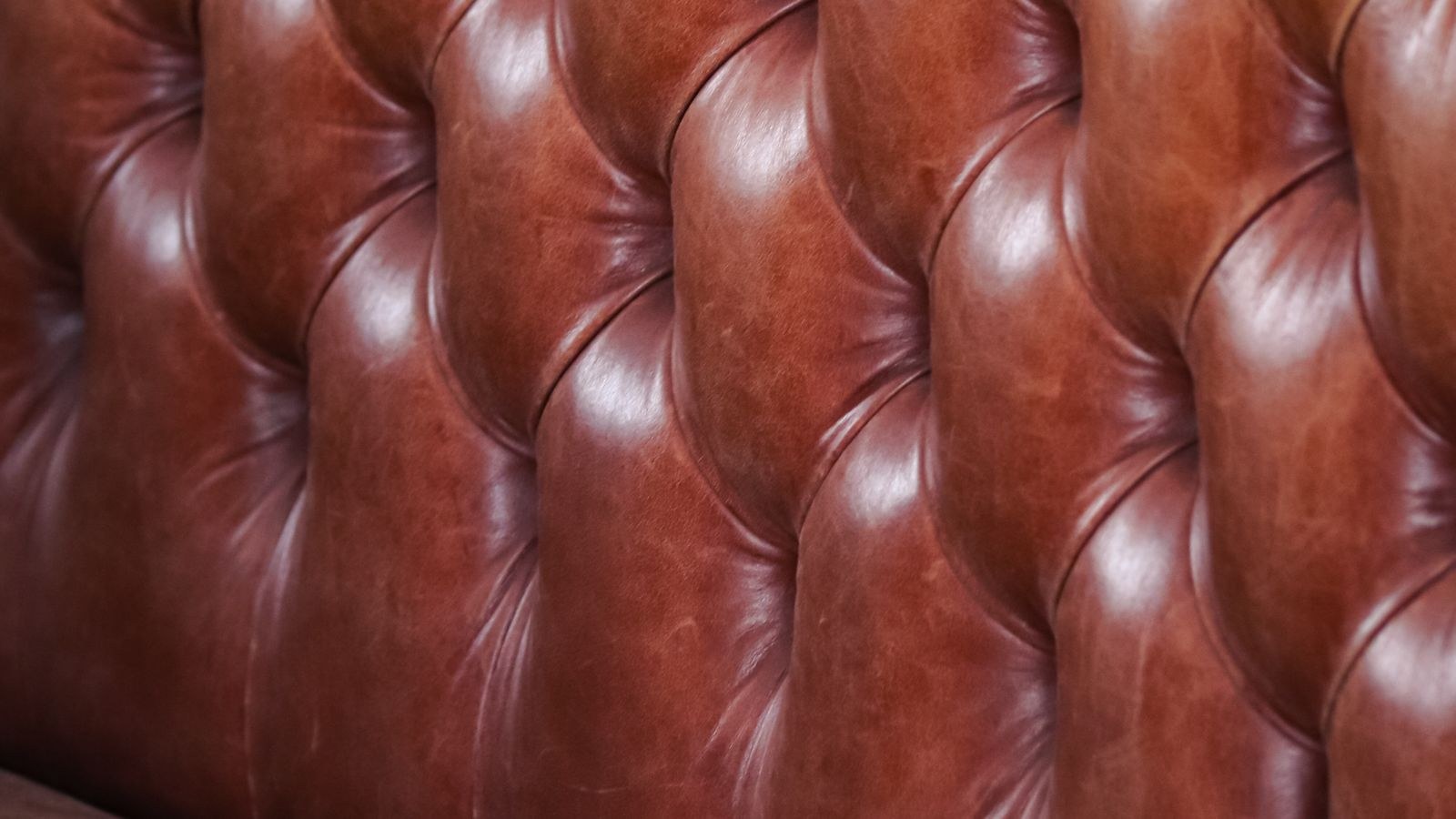 Close-up of tufted brown leather sofa upholstery showing grain texture