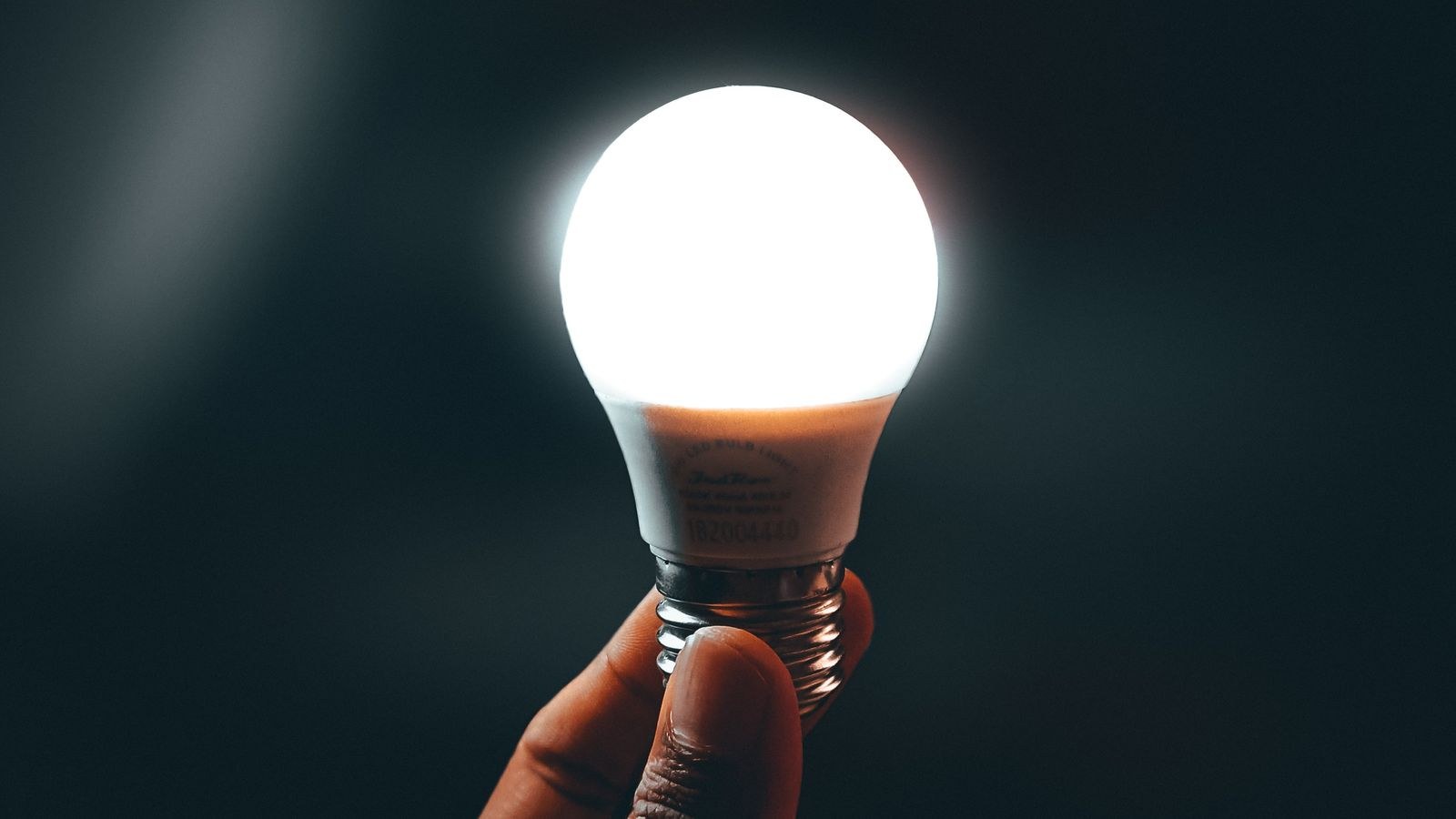 Hand holding a bright LED light bulb against a dark background