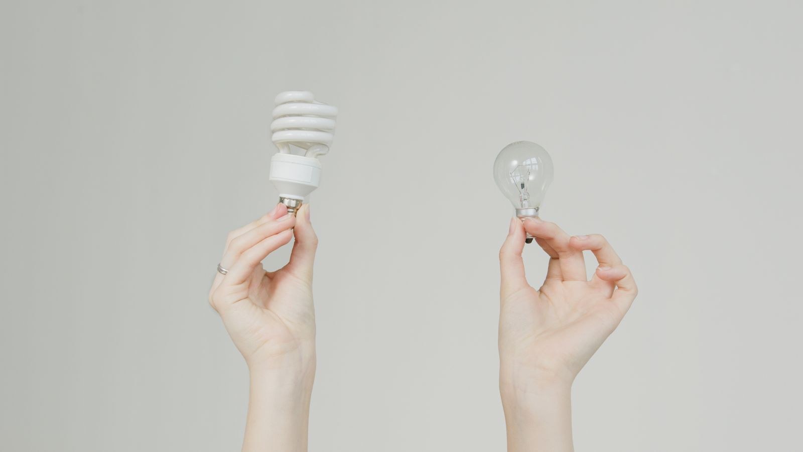 Hands holding an incandescent bulb and a spiral CFL comparing energy efficiency