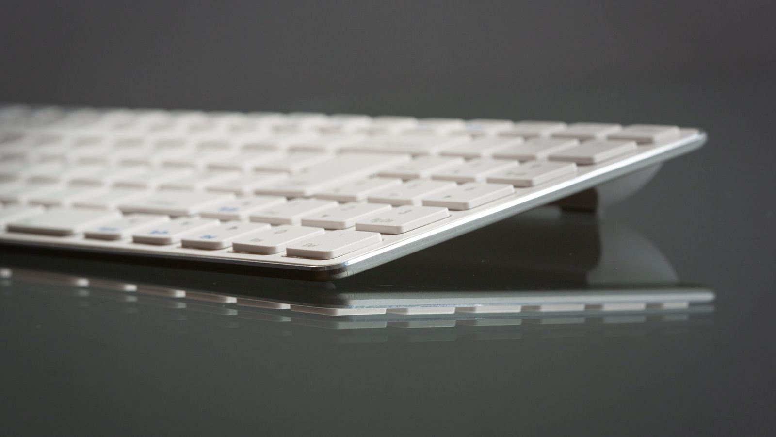 Minimalist slim keyboard photographed on a reflective surface showing low key height