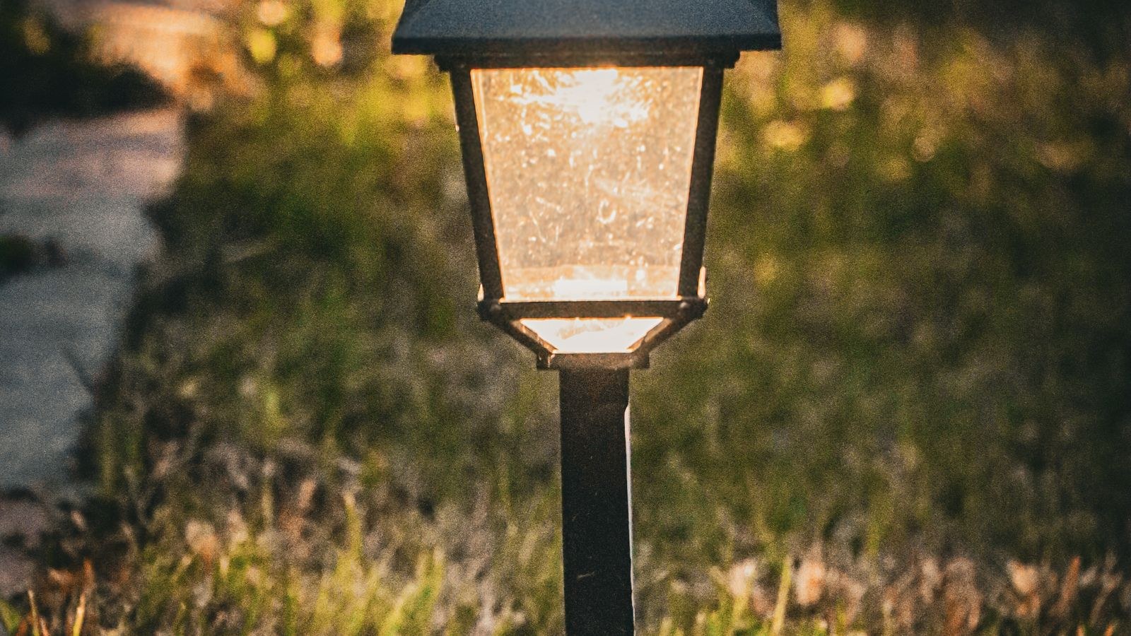 Solar garden light glowing beside a pathway in the evening