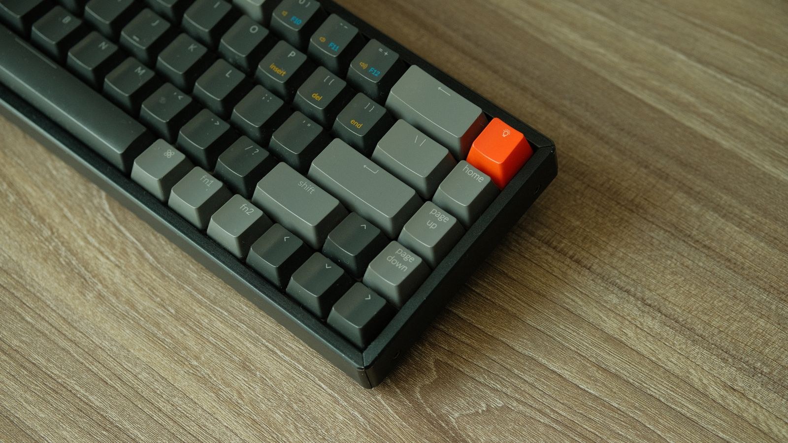 Close up of a mechanical keyboard with an orange accent keycap on a wooden table