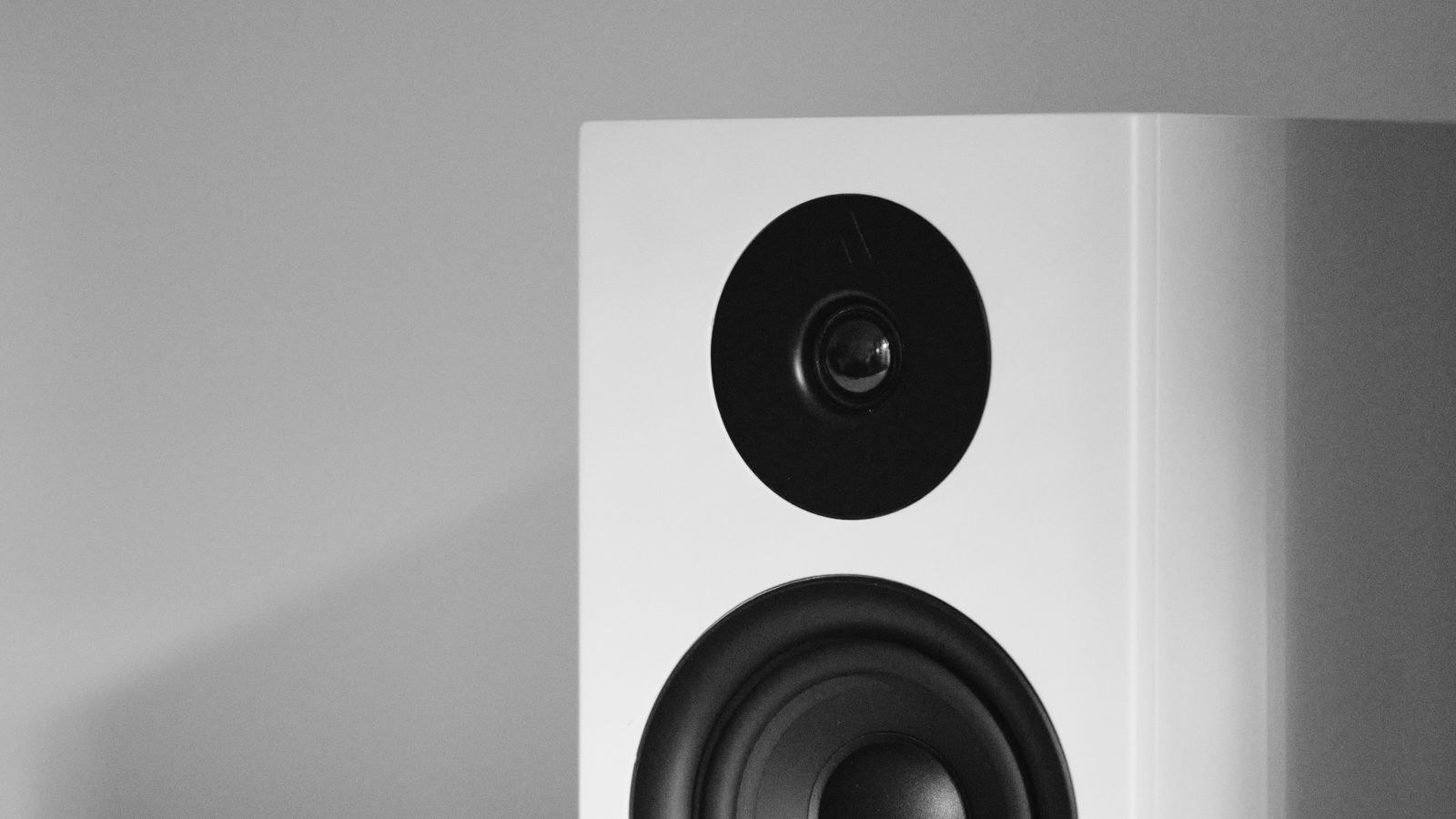 Minimalist white loudspeaker mounted on a wall shelf in a home interior